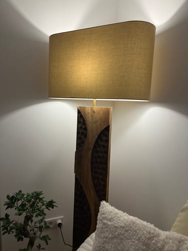Kundenfoto der beleuchteten Holz-Stehlampe AMAZONIA mit großem Leinenschirm, die in einer Zimmerecke steht.