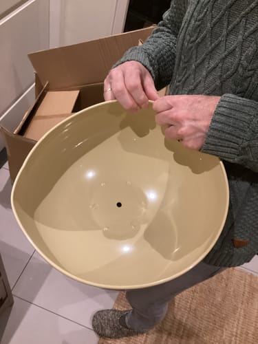 Klant houdt het komvormige, beige tafelblad van de Luna bijzettafel vast na het uitpakken.