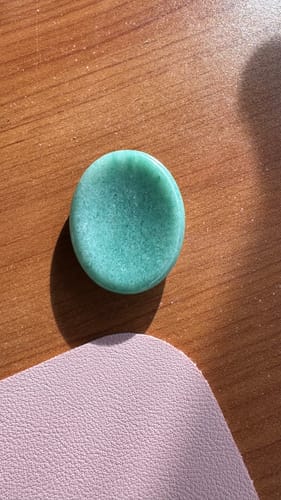 Photo d'un client montrant sa pierre anti-stress Aventurine. La pierre verte est lisse et posée sur une table.