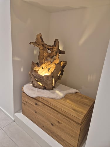Kunde zeigt die beleuchtete Treibholz Tischlampe KRYTON in einer Nische auf einer Holztruhe.