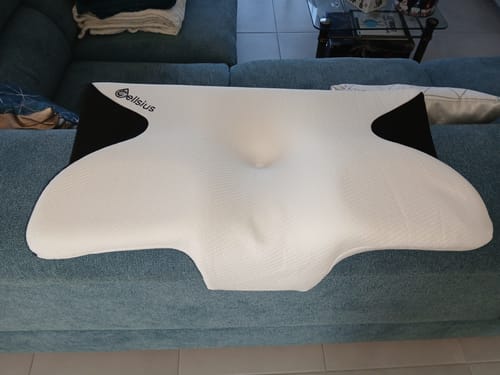 Un client montre le coussin d'alignement cervical Cellsius de forme ergonomique sur un canapé.
