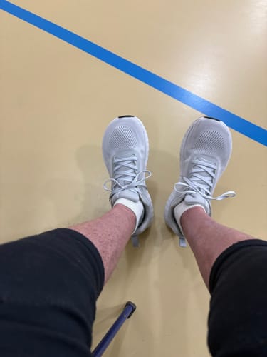 Reviewer's top-down view of their light-colored MUUV Flow pickleball shoes on a court, showing the wide toe box.