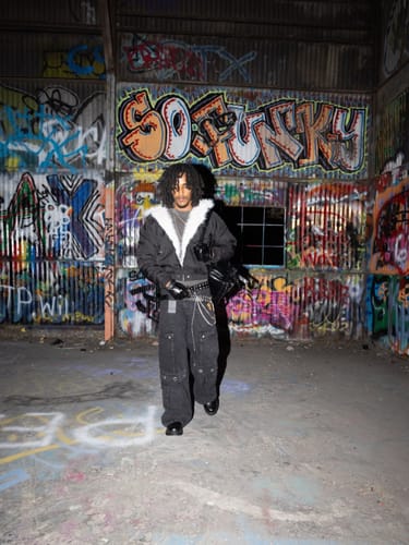 Reviewer wears the black Bomber Jacket with a white fur collar in a graffiti-covered warehouse.