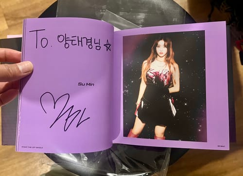 Reviewer holding the STAYC SO BAD signed album open to a purple page with Su Min's photo and personalized signature.