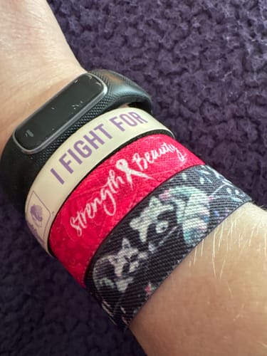 Reviewer's wrist stacked with bracelets, including the red 'Strength & Beauty' band and a watch.
