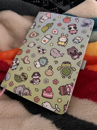 Reviewer's Mixed Characters Daily Planner with its cute illustrated cover, lying on a soft, colorful blanket.