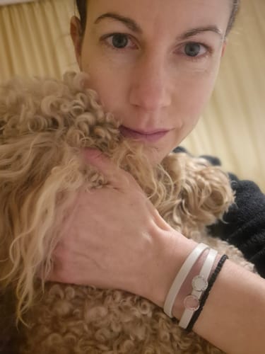 Customer wearing the white Liora bracelet with two round charms on their wrist while holding a dog.