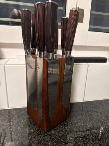 Rezensent zeigt ein Messerset mit Holzgriffen in einem Messerblock aus Holz auf einer Arbeitsplatte.