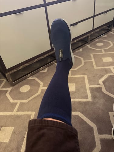 Customer wearing a navy blue Performance Eucalyptus Compression Sock pulled up to their knee indoors.