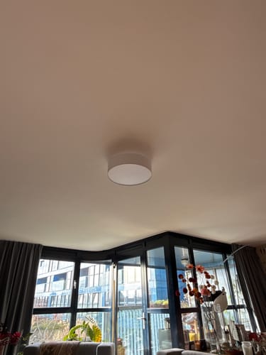 Klant toont de eenvoudige, witte Drum LED plafondlamp gemonteerd aan het plafond in een woonkamer.