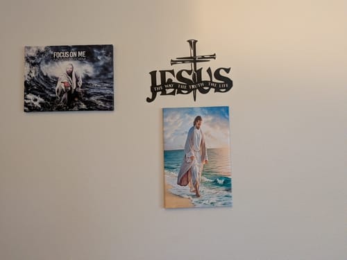 Customer's black Jesus & Cross metal wall decor displayed on a gallery wall with other religious pictures.