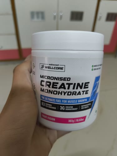 Customer holding a white tub of Wellcore Micronised Creatine Monohydrate in the Fruit Fusion flavor.