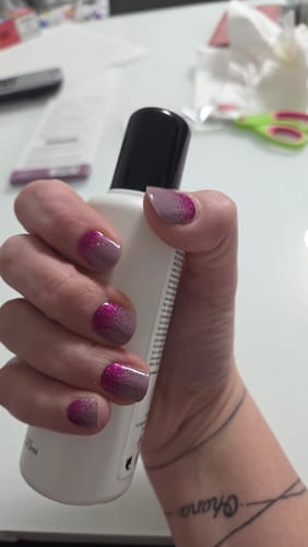 Hand einer Kundin, die eine Flasche hält und die Time To Party UV Gel Wraps mit pinkem Glitzer-Ombré-Design zeigt.