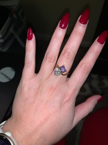 Customer's hand wearing the gold Navae Birthstone Ring with its clear pear-cut and purple radiant-cut stones.