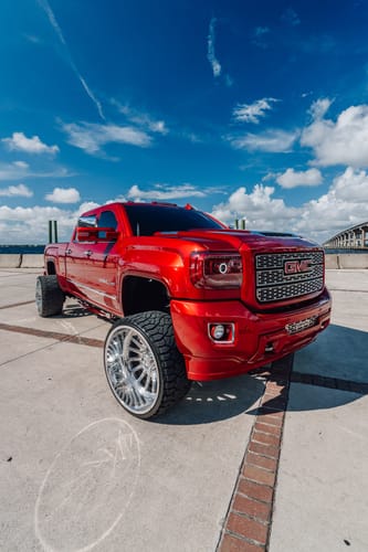 Customer's image of a shiny red GMC truck with large chrome wheels parked under a blue sky.
