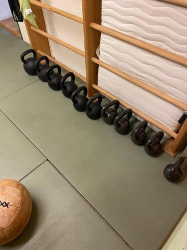 Customer's collection of black Strength Shop Cast Iron Kettlebells lined up by size on a gym mat.