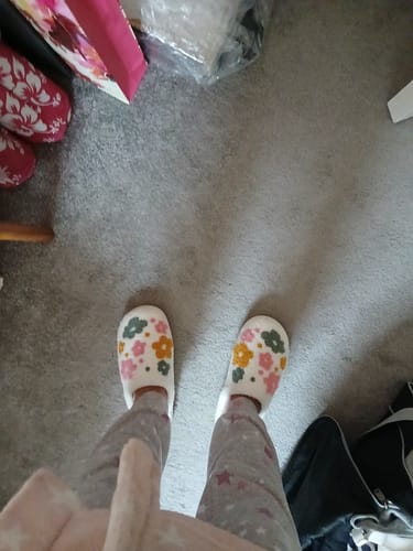 A customer's view looking down at their feet in the comfortable Livia Flower Slippers with a colorful floral pattern.