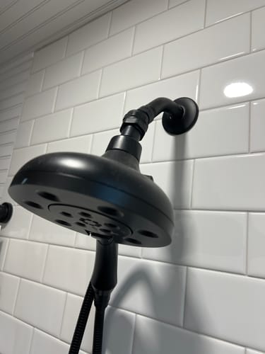 Customer's black Shower Head Swivel Adapter angling a large shower head down in a tiled shower.
