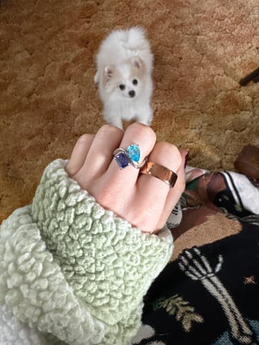 Customer's hand wearing the Navae Birthstone Ring with a dark blue radiant-cut stone and a light blue pear-cut stone.