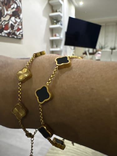 Reviewer's arm wearing two gold-colored bracelets with black and gold clover-shaped charms.