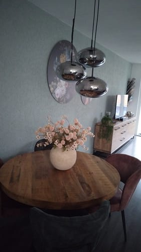 Klant toont het crème wax arrangement in een pot op een ronde, houten eettafel.