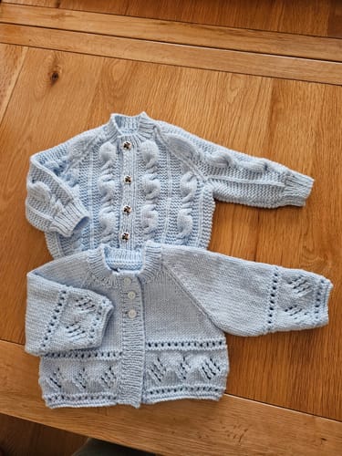 Reviewer shows two finished light blue baby cardigans knitted with the wool from the kit.