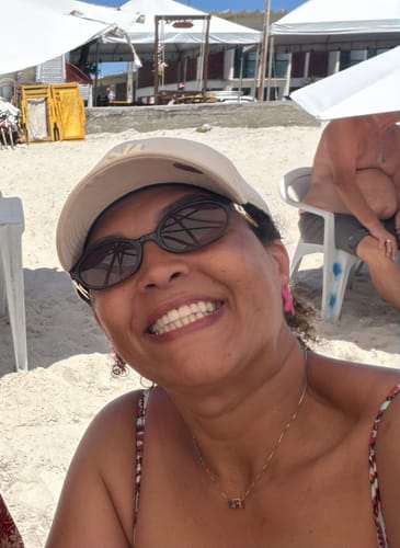 Cliente sorrindo na praia, usando os Óculos Brescia com armação oval escura.