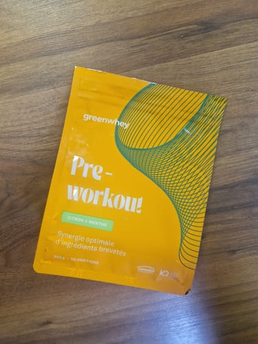 Client montrant le sachet jaune de Pre-Workout saveur citron et menthe, posé sur un sol en bois.