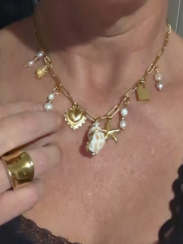 Close-up of a reviewer showing their gold charm necklace and thick gold ring.