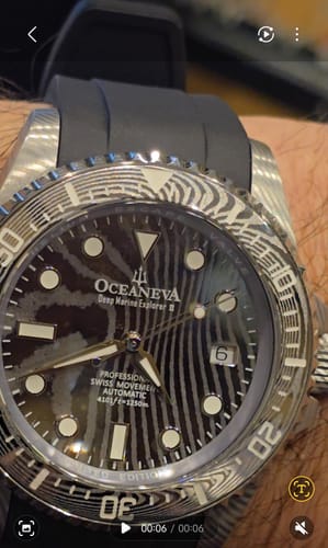 Close-up of a reviewer wearing the Oceaneva watch, highlighting the wavy Damascus steel pattern on the dial and bezel.