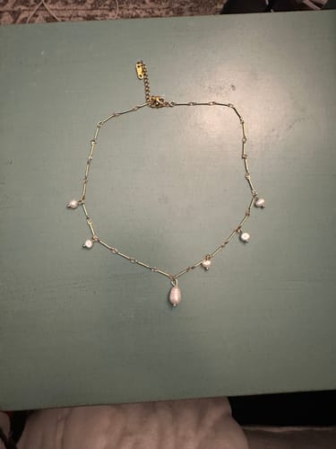 Customer's Santorini Pearl Necklace laid out on a flat green surface, showing the delicate gold chain and pearls.