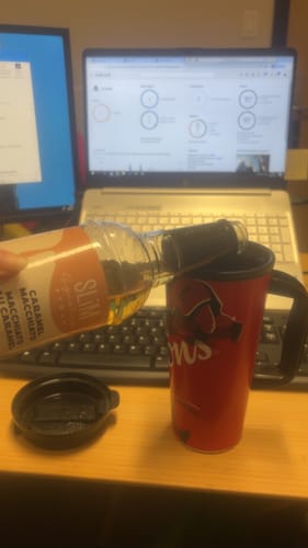 Client versant du sirop Slim Syrups d'une bouteille dans une tasse de voyage rouge sur un bureau.