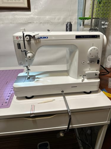 Reviewer's Juki TL-2010Q Quilting Machine on a white desk, with the knee lifter attached and light on.