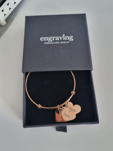 Customer's gold Heart Pendant Bracelet with two engraved heart charms resting in its black presentation box.