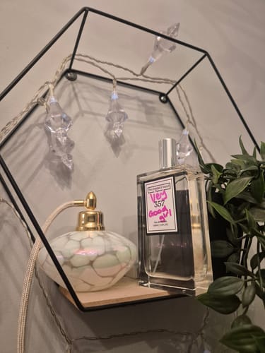 Customer's Inspired By Very Good Girl - 357 perfume bottle on a decorative, hexagonal shelf next to a vintage atomizer.