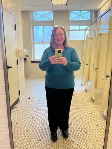 Reviewer in a mirror selfie showing the fit of the teal Francesca Sweater paired with black pants.