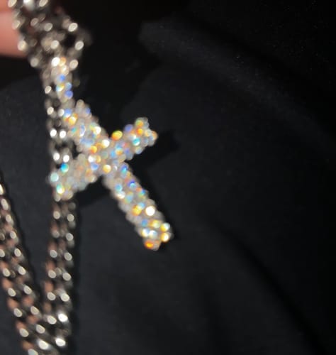 Close-up: Customer's sparkling Moissanite Cross Pendant on a silver chain against a dark surface.