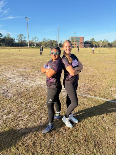Two reviewers posing back-to-back on a soccer field in their custom black sublimation soccer jerseys.