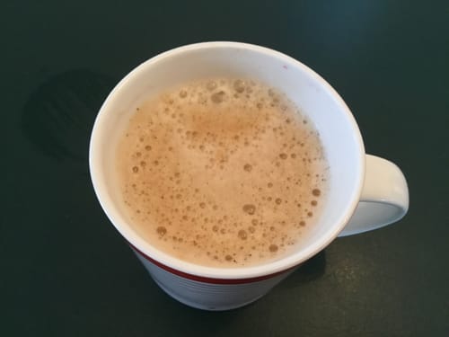 Customer's frothy Caramel Blend coffee served in a white mug with a red stripe.
