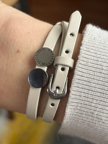 Customer's wrist wearing the off-white leather Liora bracelet with its personalized engraved charms and small buckle.