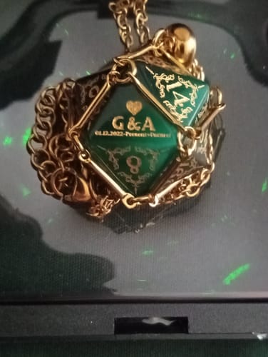 Customer's personalized green D20 anniversary dice held in a gold-colored cage as a necklace.