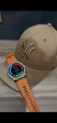 Customer's Gard Pro Ultra 3 watch with an orange band, resting on a tan baseball cap with the screen showing activity metrics.