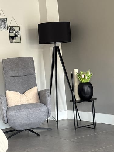 Recensent toont de zwarte Zuiver Tripod vloerlamp in een stijlvolle leeshoek naast een fauteuil.
