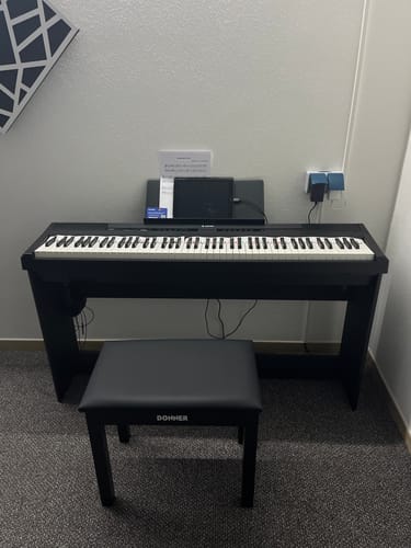 Ein Kunde zeigt sein schwarzes Digitalpiano Donner DEP-20, das mit einer passenden Bank in einem Raum aufgestellt ist.