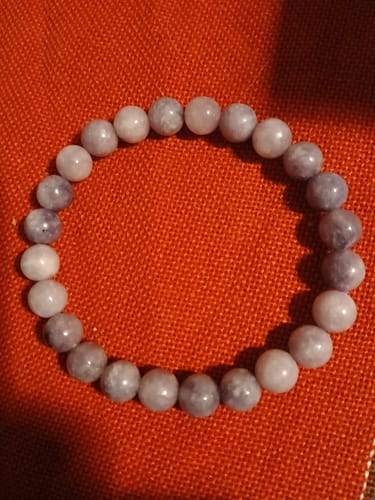 Photo d'un client montrant un bracelet Lépidolite avec des perles violettes et roses sur un tissu rouge.