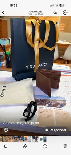 Cliente exhibe su Billetera Gante Café abierta sobre una mesa, junto a su bolsa de compra y funda de tela.