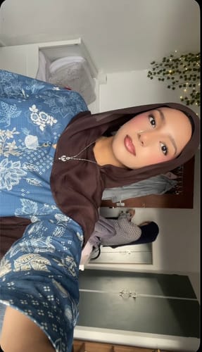 Reviewer wearing the Dark Chocolate Premium Modal hijab indoors over a blue patterned top.