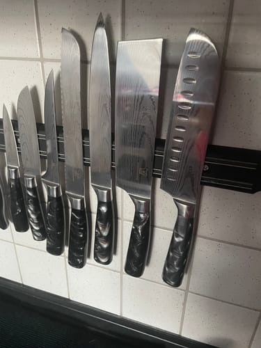 Rezensent zeigt das Kuro Messerset mit schwarzen Griffen, das an einer Magnetleiste in einer weiß gefliesten Küche hängt.