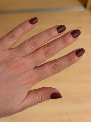 Hand einer Kundin, die die Royal Temptation UV-Gelnagelfolien in einem tiefen Weinrot mit mattem Finish trägt.