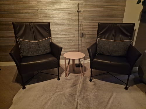 Recensent toont de crèmekleurige by fonQ Clip bijzettafel tussen twee donkere fauteuils.